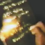 close-up of a hand writing in chalk on a black board, lit by a flashlight